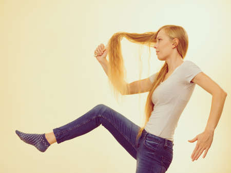 Blonde woman with brush combing her very long hair. Teenage girl taking care refreshing her hairstyle. Haircare concept.の写真素材