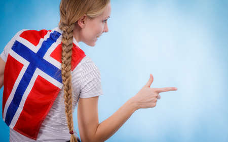 Blonde girl braid hair with norwegian flag on her back, female pointing with finger to copy space text area. Scandinavian people.の写真素材