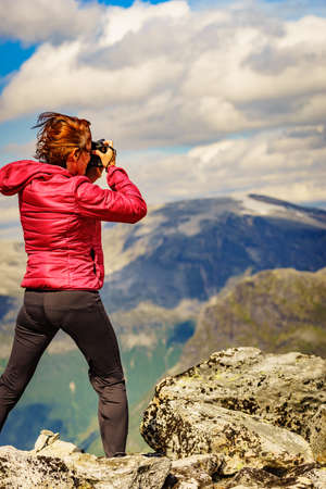Tourism vacation and travel picture. Female tourist taking photo with camera, enjoying nature from Dalsnibba mountain viewpoint at windy day, Norway.の写真素材