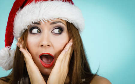 Woman wearing santa claus hat surprised expression, on blue with copy space. Christmes time.の写真素材