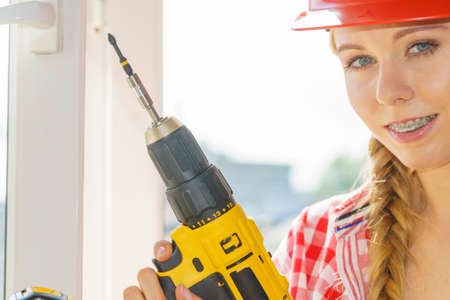 Young woman adjusting, changing her drill bit doing home renovation. Female construction worker having driller tool working on diy.の写真素材