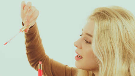 Happy cheerful woman is about to use red tinted lips gloss on her lip. Make up concept.の写真素材