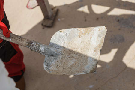 Unrecognizable person worker using shovel standing on industrial construction site, working hard on house renovation.の写真素材
