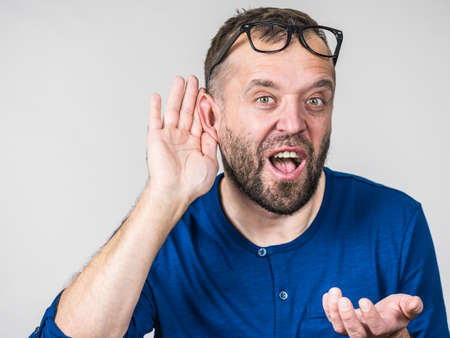 Man in eyeglasses having troubles with hearing, being deaf. Guy gesturing eavesdropping with hand...