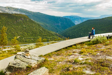 Woman with camera resting taking photo from Vedahaugane bench rest stop. National Tourist Route...