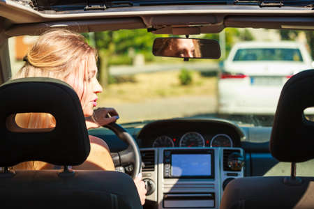 Young blonde woman driving car, view from rear seat