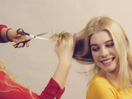 Hairstyle and haircut. Young female barber holding scissors tool ready to trimming hair her friends. Two girls creating new hairdo coiffureの写真素材