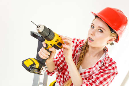 Young determinated woman using drill doing home renovation. Female construction worker having...