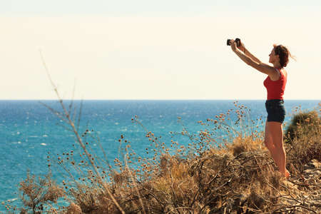 Tourist adventurous adult woman exploring nature and taking pictures using professional camera. Freelancer travel photographer next to sea.の写真素材