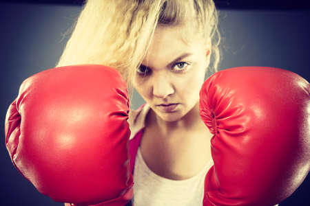 Sporty angry determined woman wearing red boxing gloves, fighting. Studio shot on dark background.の写真素材