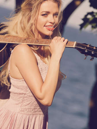 Hippie looking young adult woman wearing gypsy outfit having acoustic guitar. Female playing music in park.の写真素材