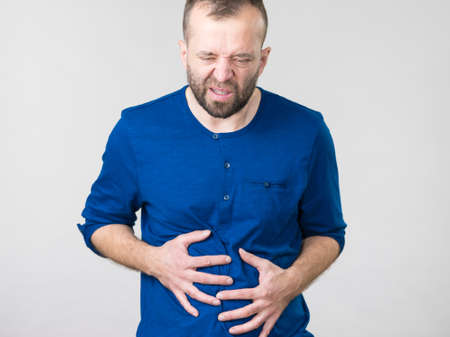 Man having huge stomach pain holding his belly feeling very unwell. Guy being sick and unhealthy.の写真素材