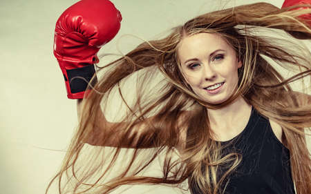 Bloned long hair girl boxer in big fun red gloves playing sports boxing. Female fight for equal rights for women.の写真素材