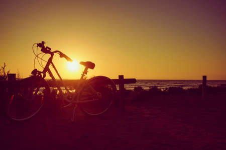 Bicycle outdoor parked on beach, evening time, sunset sky. Holidays, sport and recreation.の写真素材