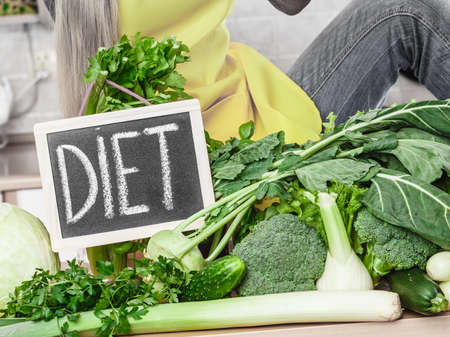 Kitchen table with many green vegetables, diet sign on blank board standing next to.の写真素材
