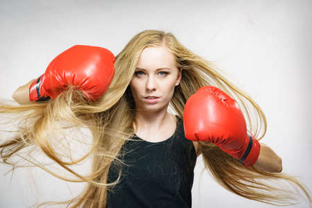 Bloned long hair girl boxer in big fun red gloves playing sports boxing. Female fight for equal rights for women.の写真素材