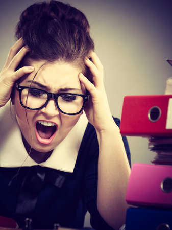 Mobbing at work, bad job relations concept. Depressed businesswoman being sad and tired sitting working at desk full off documents in binders.の写真素材