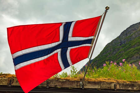 Sod roof hause and norwegian flag waving outdoor on green nature, mountains in the background