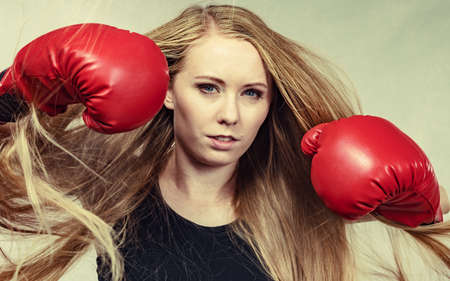 Bloned long hair girl boxer in big fun red gloves playing sports boxing. Female fight for equal...