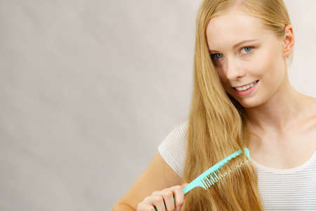 Blonde girl with comb brushing her long hair. Girl taking care refreshing her hairstyle. Haircare concept.の写真素材