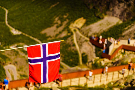 Trollstigen mountain road landscape in Norway, Europe. Norwegian flag waving and many tourists people on viewing platform in background. National tourist route.の写真素材