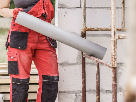 Woman in dungarees carrying plastic pipes on her home construction site, building new home.の写真素材