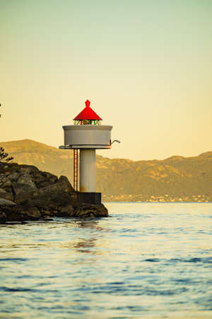 Red white lighthouse on the edge of rocky sea coast, Norwayの写真素材