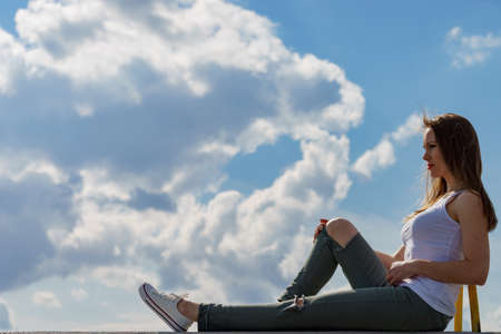 Trendy fashionable woman relaxing outdoor wearing casual footwear white sneakers and hole trousers. Female enjoy sunlight against blue sky.の写真素材