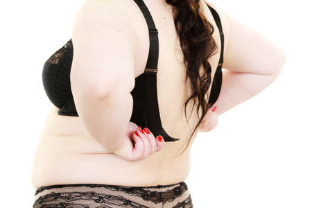Fat woman rear view opening taking off or putting on her bra. Plus size overweight female model wearing black lingerie. Bosom, brafitting and underwear concept.の写真素材