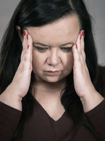 Headache, migraine and stress. Worried plus size adult upset woman suffering from head pain, studio shot on gray.の写真素材