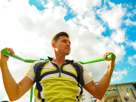Young handsome man working out in outdoor gym. Sporty guy flexing his muscles on machine. Staying...