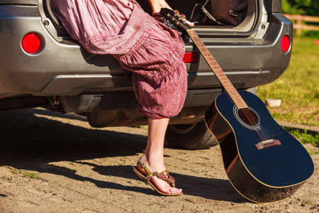 Travel vacation hitchhiking concept. Summer girl hippie style sitting on hatchback car with acoustic...
