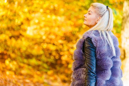 Woman wearing fashionable outfit artificial fur coat walking in autumnal park.の写真素材