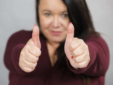 Adult happy big woman making thumb up gesture showing cool sign, on grey. Satisfaction success...