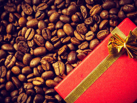 Red small gift box with bow on roasted brown coffee beans background.の写真素材