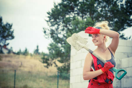 Woman worker using shovel standing on industrial construction site, working hard on house renovation.の写真素材