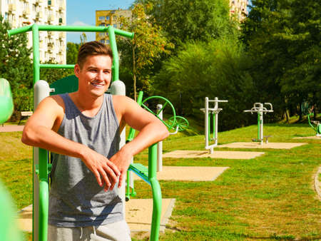 Sportsman relaxing after outdoor workout at street exercise machines for strength exercises. Fit man...