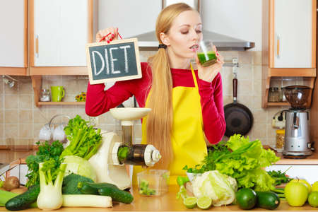 Drinks good for health, diet breakfast concept. Young woman in kitchen holding green healthy vegetable smoothie juice glass next to diet sign.の写真素材