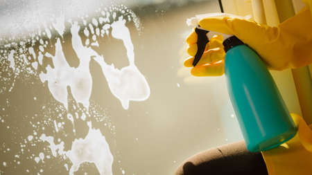 Female hand in yellow gloves cleaning window with blue rag and spray detergent. Spring cleanup, housework conceptの写真素材