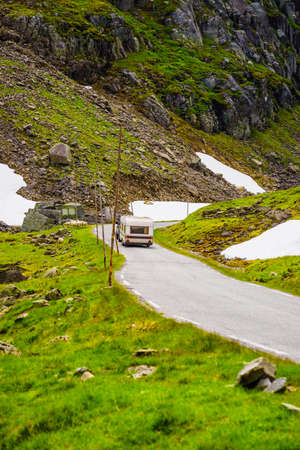 Car with trailer drive on road across green summer norwegian mountains. Travel, holidays and adventure concept.の写真素材