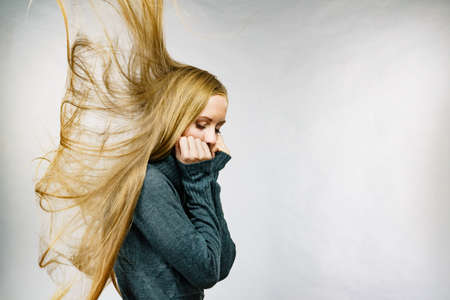 Sad girl with blowing long blonde hair wearing warm sweater clothing. Copy spaceの写真素材