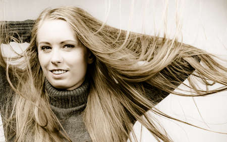 Smiling girl with blowing long blonde hair wearing warm sweater clothing.