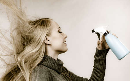 Girl messy long dry hair holding bottle, applying thermal protect hair spray.
