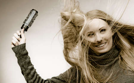 Blonde woman styling her very long hair. Teenage girl with blowing messy hair holding hairbrush.の写真素材