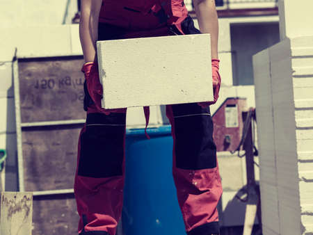 Unrecognizable woman working on construction site, building house, installing gray airbricks. Industrial work concept.の写真素材