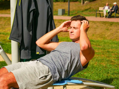 Young man working out in outdoor gym. Sporty guy doing abs exercises on machine. Staying fit and...