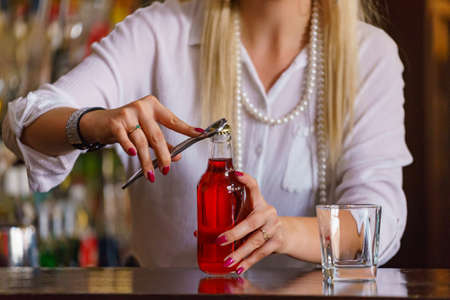 Woman working at the bar counter, holding red bottle lemonadeの写真素材