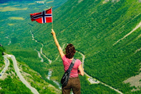 Tourist woman with norwegian flag on Trollstigen viewpoint. Trolls Path mountain road in Norway. National route. Touristic attraction.の写真素材
