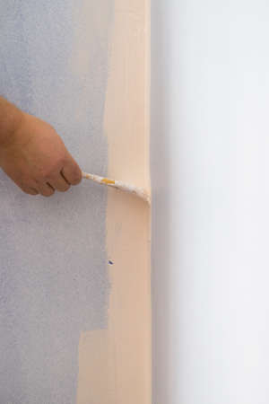 Person appplying white paint on blue wall using brush. Home renovation concept.の写真素材