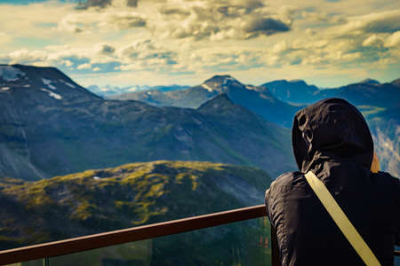 Tourist standing on Dalsnibba viewpoint, Geiranger Skywalk platform, enjoying mountains view,...